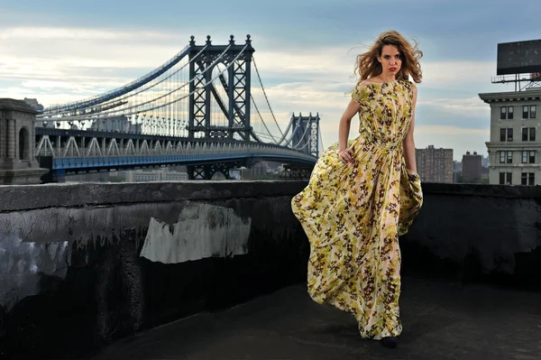 Modelo de moda posando sexy, vestindo vestido de noite longa no telhado localização com construção de ponte de metal no fundo — Fotografia de Stock