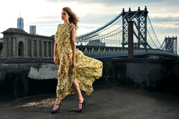 Fashion model poseren sexy, lange avond jurk dragen op dak locatie met metalen bruggenbouw op achtergrond — Stockfoto