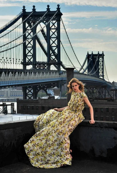 Μόδα μοντέλο Ποζάροντας σέξι, φορώντας μακρύ βραδινό φόρεμα την τοποθεσία στον τελευταίο όροφο με την κατασκευή μεταλλικών γεφυρών σε φόντο — Φωτογραφία Αρχείου