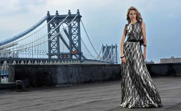 Fashion model posing sexy, wearing long evening dress on rooftop location with metal bridge construction on background Stock Picture