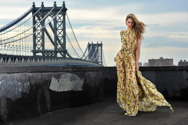 Fashion model posing sexy, wearing long evening dress on rooftop location with metal bridge construction on background Royalty Free Stock Photos