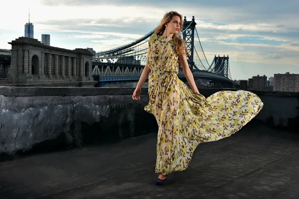 Fashion model posing sexy, wearing long evening dress on rooftop location with metal bridge construction on background Royalty Free Stock Images