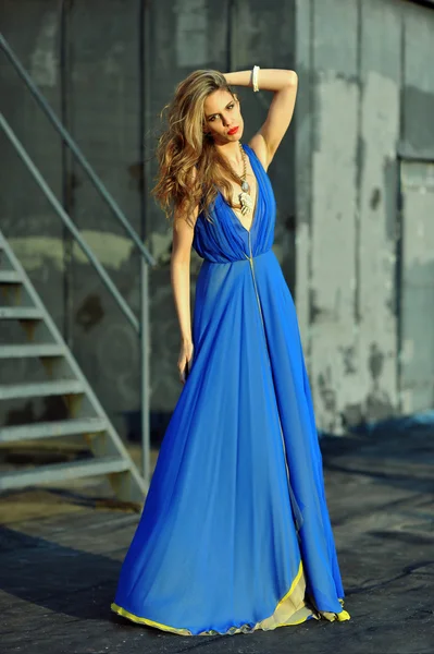 Moda modella posa sexy, indossa lungo abito da sera blu sulla posizione sul tetto — Foto Stock
