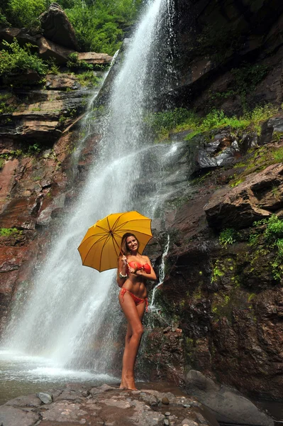 Dívka pózuje před vodopády s žlutým deštníkem — Stock fotografie