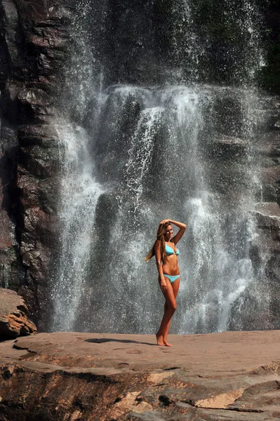 Beautiful slim fitness model posing sexy in front of waterfalls — Stock Photo, Image