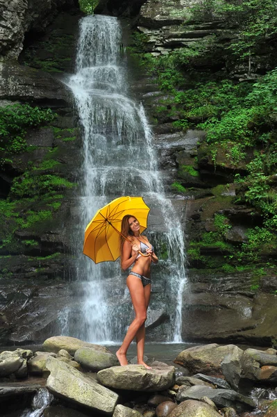 Girl posing in front of waterfalls with yellow umbrella — Stock Photo, Image