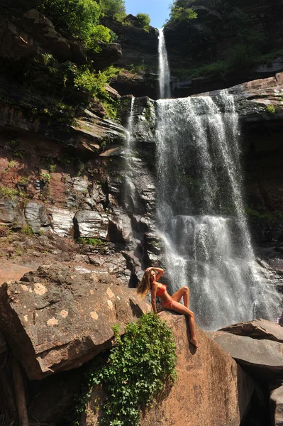 Beautiful slim fitness model posing sexy in front of waterfalls — Stock Photo, Image