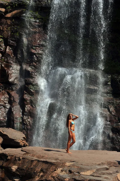 Beautiful slim fitness model posing sexy in front of waterfalls — Stock Photo, Image