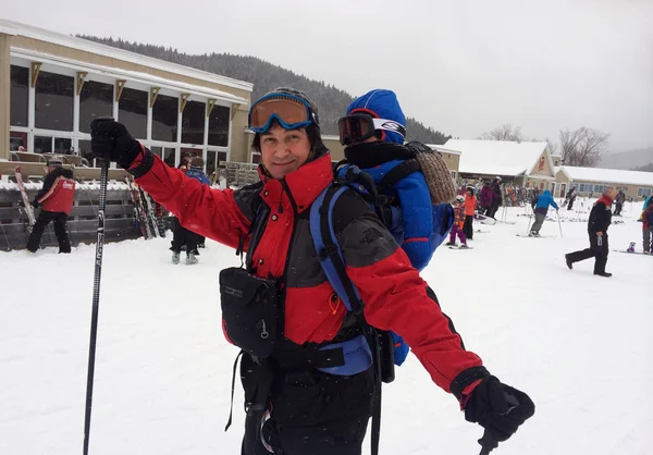Glad skidåkare med kid i ryggsäck — Stockfoto