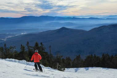 Back view of the skier in red jacket riding down the slope in Stowe mountains. Winter sport. Vermont, USA. Beautiful mountains, winter landscape.