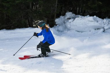 Female skier in bright blue jacket riding downhill on fresh powder snow. Sport and lifestyle concept.
