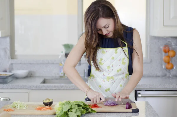 Krásná brunetka v kuchyni řezání zeleniny — Stock fotografie