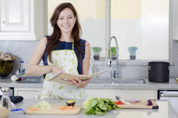 Mulher bonita consultar um caderno enquanto cozinha — Fotografia de Stock