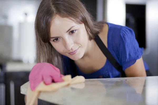 Gelukkig jonge huisvrouw in roze handschoenen reinigen een glazen tafel in de keuken — Stockfoto