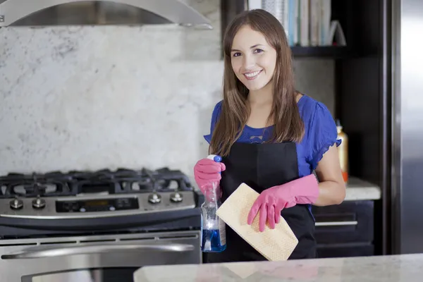 Pembe eldivenleri ve siyah önlük ayakta tutarak toz bezi ve temizleyici mutfakta genç gülümseyen kadın