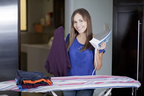 Happy young woman ironing on ironing board at home, smiling. — Stock Photo, Image