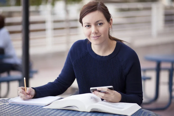 Beautiful young woman sitting by table and studying — Stock Photo, Image