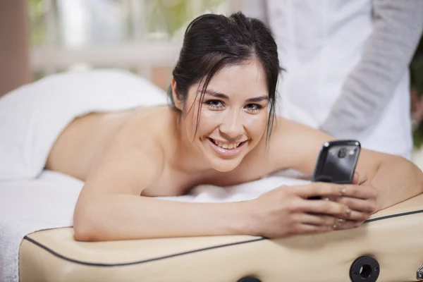 Mulher digitando mensagem em seu celular enquanto tem massagem — Fotografia de Stock