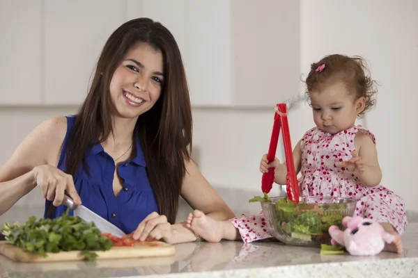 Брюнетка мать помогает дочери готовить салат на кухне — стоковое фото
