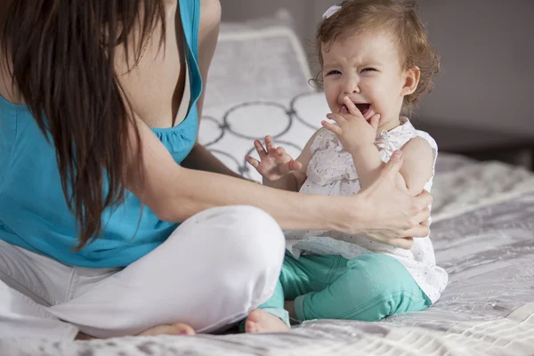 Brunette vrouw spelen met haar baby op een bed in haar appartement — Stockfoto