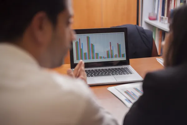 Businessman and businesswoman sitting at desk at work, looking at laptop — Stock Photo, Image