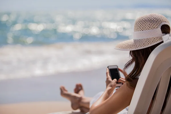 Jonge vrouw met mobiele telefoon op een strand Stockafbeelding