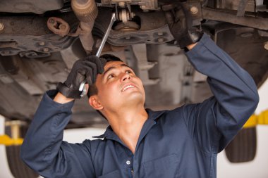 Car mechanic examining car suspension of lifted automobile at repair service station clipart
