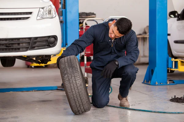 Mecánico masculino en un garaje de coches que fija una rueda —  Fotos de Stock