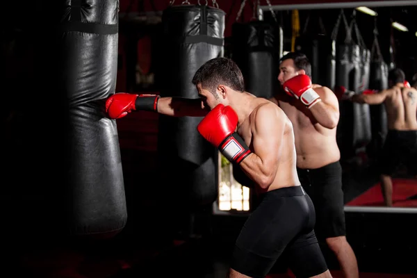 Entrenamiento de boxeador joven con saco de boxeo en gimnasio con entrenador personal — Foto de Stock