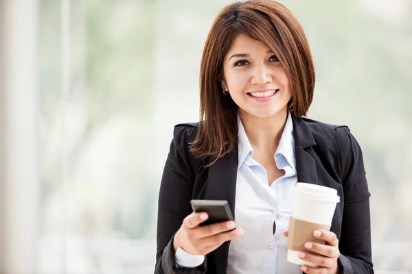 Mooie glimlach zakelijke vrouw texting op haar mobiele telefoon en holding een kop van koffie — Stockfoto