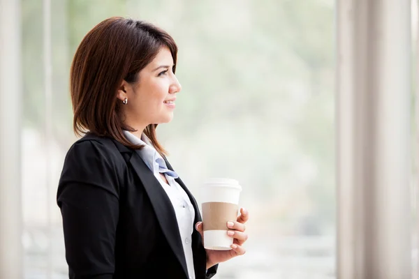 Atrakcyjny biznes młoda kobieta patrząc w okno i holdng filiżankę kawy — Zdjęcie stockowe
