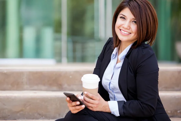 Empresária sorridente sentada na escada com café e um telefone olhando para a câmera — Fotografia de Stock