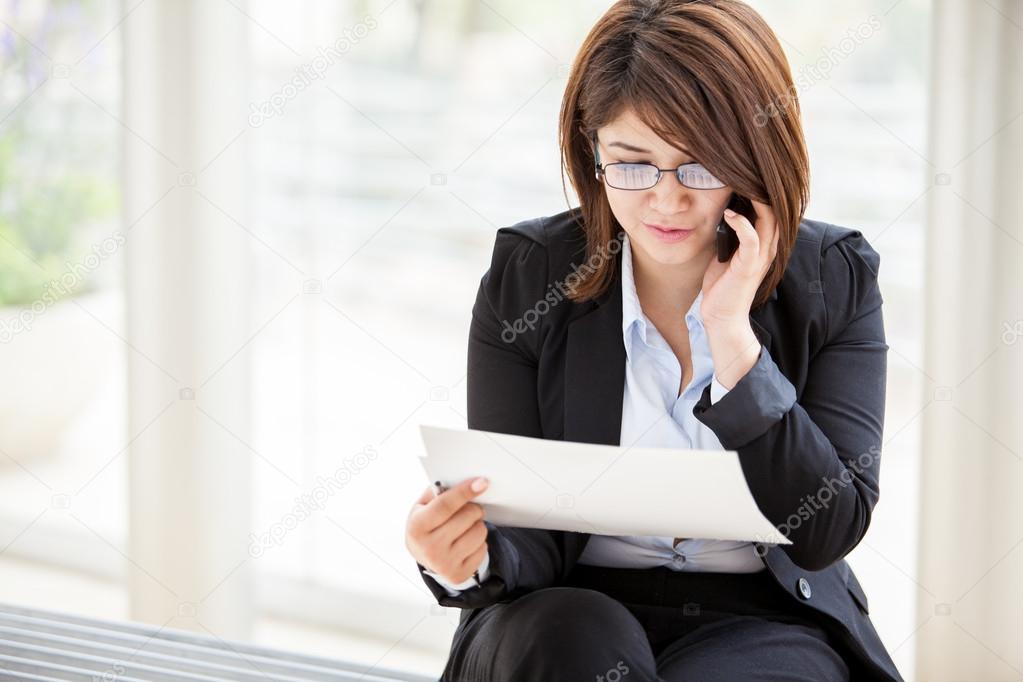 Beautiful business woman looking at papers she holding in her arms while calling on her phone