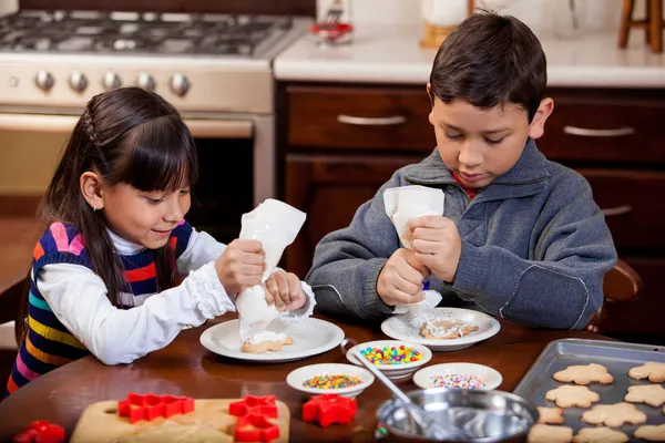 Siblings putting frosting on some holiday cookies — Stock Photo, Image