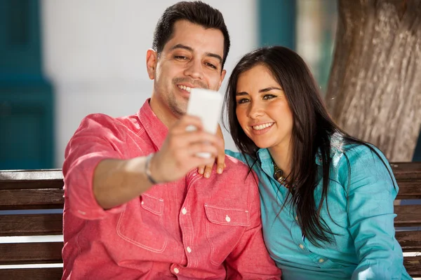 Linda pareja tomando fotos de sí mismos mientras están sentados en el banco en el parque — Foto de Stock