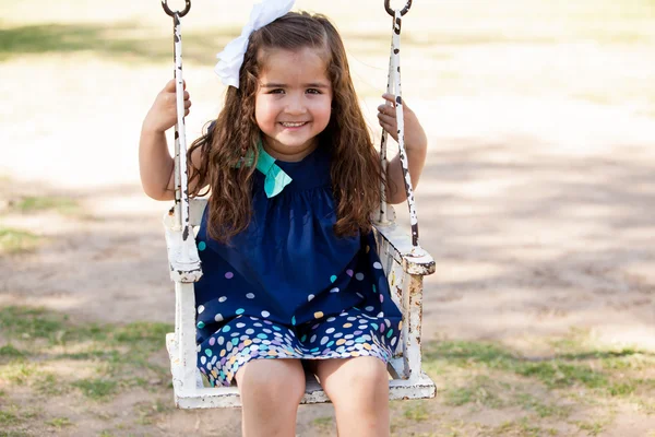 Beautiful little brunette on a swinging chair at a park — Stock Photo, Image