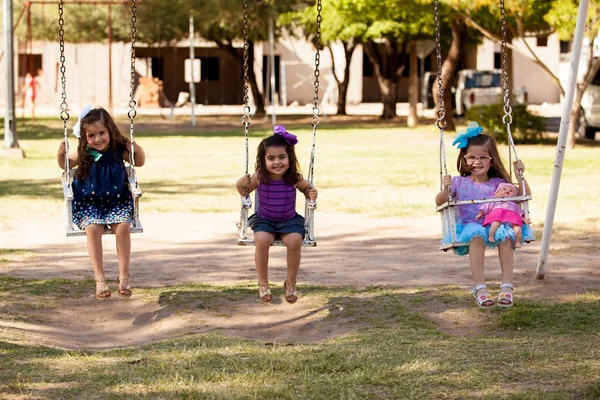 Sweet little girls having fun in a swing at a park on a sunny day — Stock Photo, Image