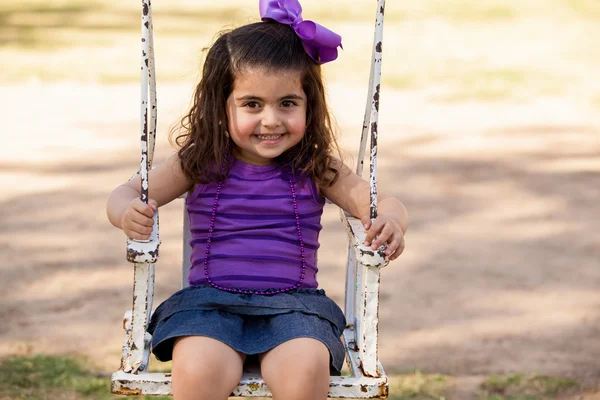 Cute little Latin girl having fun on a swing at a park and smiling — Stock Photo, Image