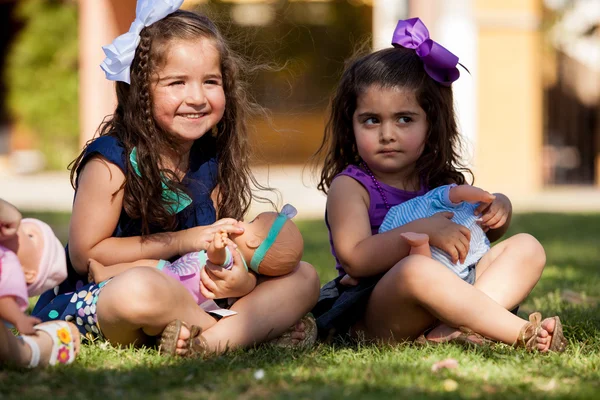 Pretty little girls having fun and playing with their dolls at a park — Stock Photo, Image