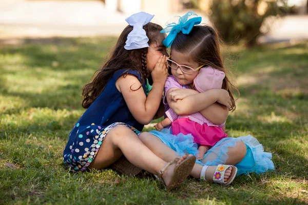 Beautiful little brunette telling her friend a secret while relaxing at a park — Stock Photo, Image