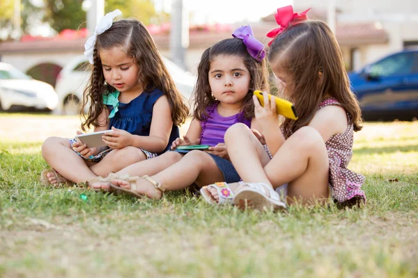 Pretty little girls playing with their smart phones while hanging out at a park