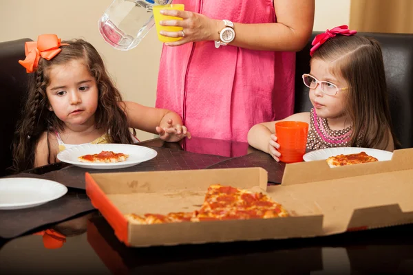 Hermosos amiguitos comiendo pizza en casa mientras una madre los supervisa y les sirve —  Fotos de Stock