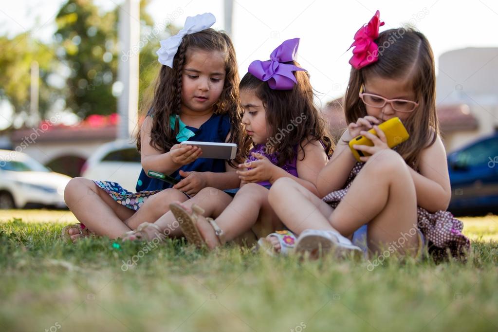 Potrait of three cute little girls each one using their own smart phone at a park