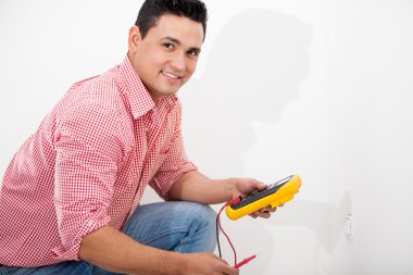genç bir İspanyol elektrikçi elektrik prizi yanındaki bir multimetre kullanarak portresi