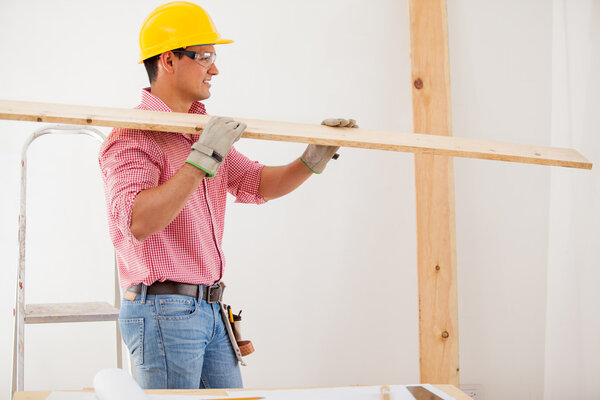 Young man wearing protective gear and carrying some wood for a constructionhouse