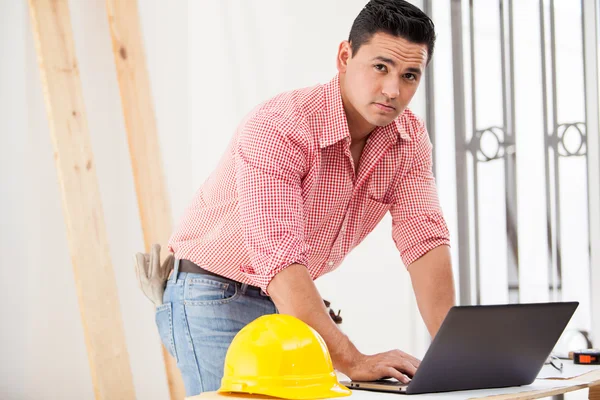 Gut aussehender hispanischer Bauunternehmer, der vor Ort an einem Laptop arbeitet — Stockfoto