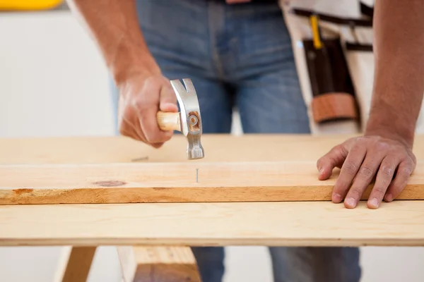 Primer plano de un contratista masculino usando un martillo en algunos clavos y madera —  Fotos de Stock