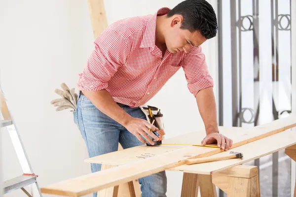 Contratante latino atraente usando uma fita métrica antes de cortar uma placa de madeira no trabalho — Fotografia de Stock