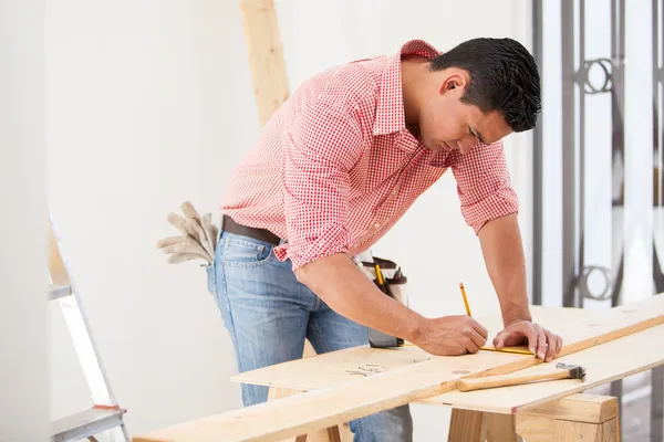 Csinos fiatal carpenter egy mérőszalag segítségével Kivágás előtt le egy fából készült hajón méretek megjelölése — Stock Fotó