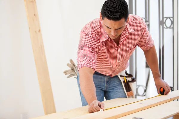 Empreiteiro hispânico masculino usando uma fita métrica em uma placa de madeira no trabalho — Fotografia de Stock